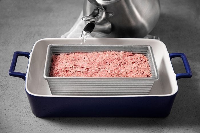 Pouring water in bigger pot with baking dish in it.