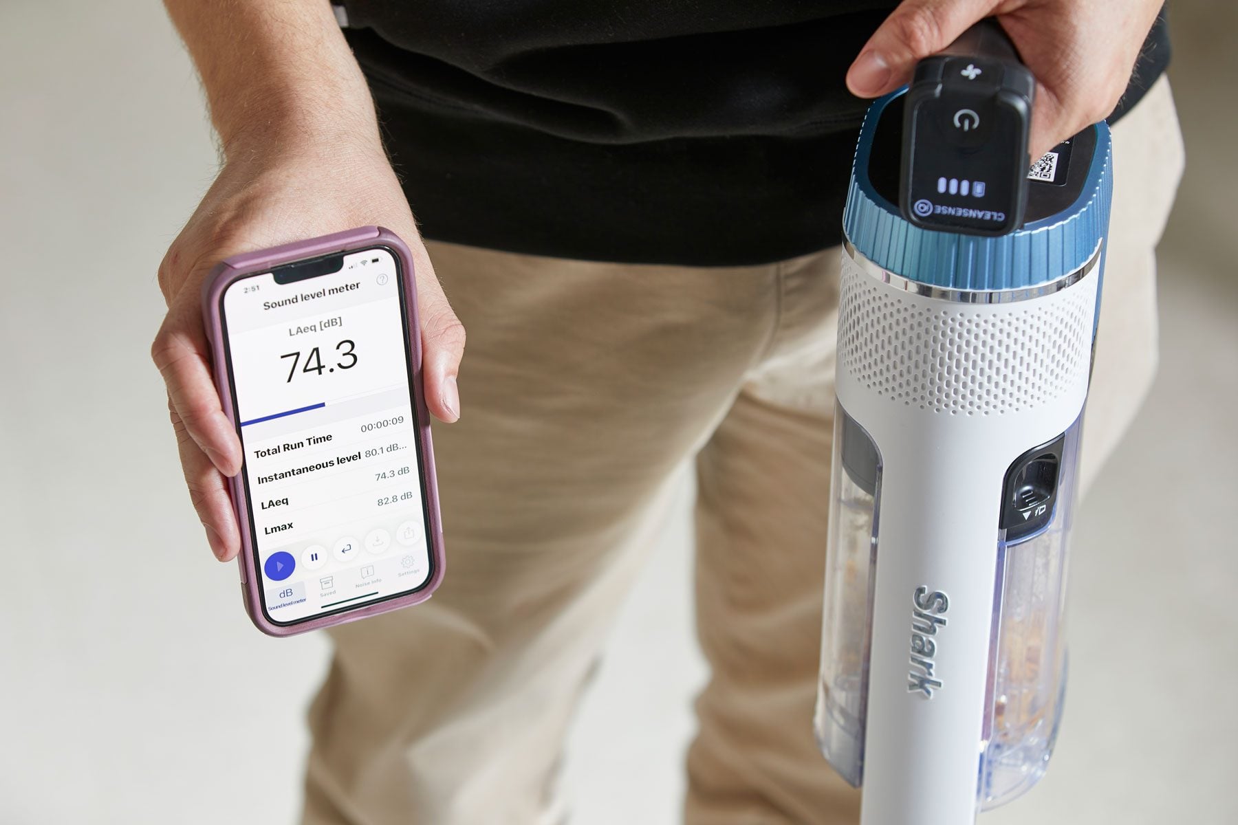 A man holding a phone showing Dyson app and hold a vacuum on the other hand