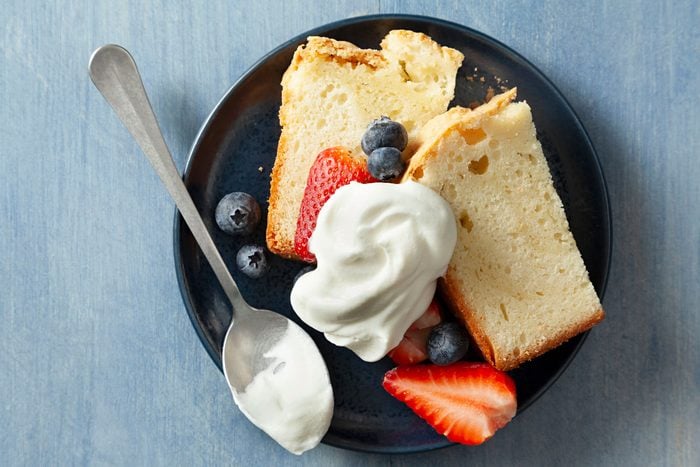 Bread and Berries Topped with Sweetened Whipped Cream Served on a black small plate placed on a textured light blue surface