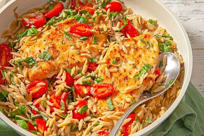 A bowl of Lemon Chicken with Orzo, topped with succulent chicken and juicy tomatoes