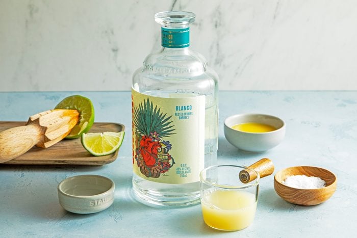 A bottle of tequila with lime slices and orange juice