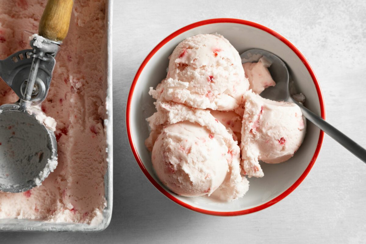 Overhead shot of Easy Strawberry Ice Cream served in bowl with spoon; ice cream container; scoop; white marble background;