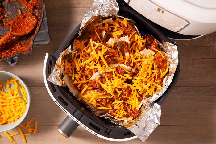 Nachos dressed and topped with cheese on foil layer in air fryer
