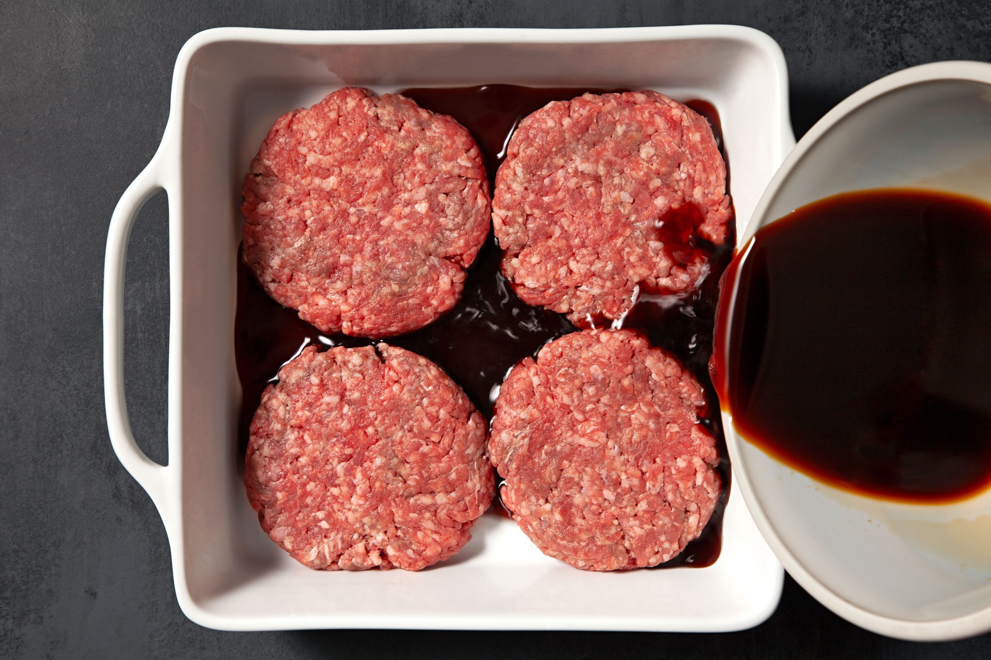 overhead shot; black background; Shape beef into 4 patties; place in an square baking dish, Pouring the remaining teriyaki sauce mixture over patties;