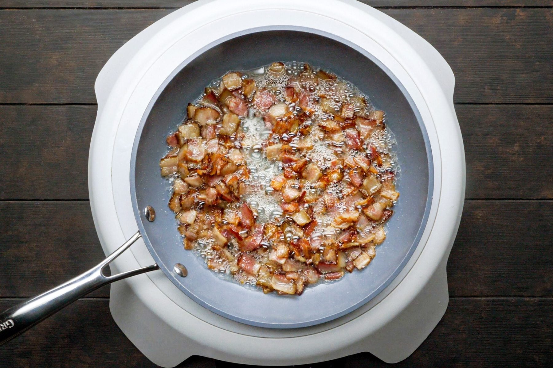 Chopped bacon is cooking in a large skillet