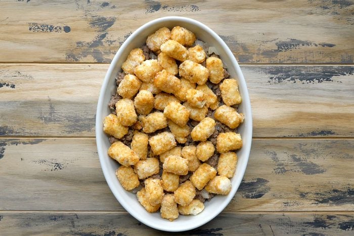 Overhead shot of transfered to a greased baking dish; top with tater tots; wooden background;