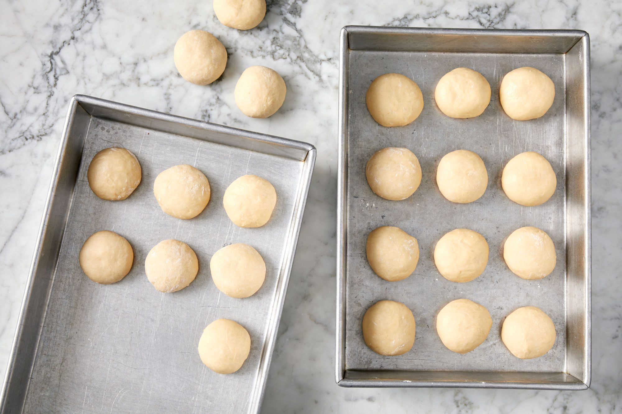 small dough balls in baking pans; marble surface;