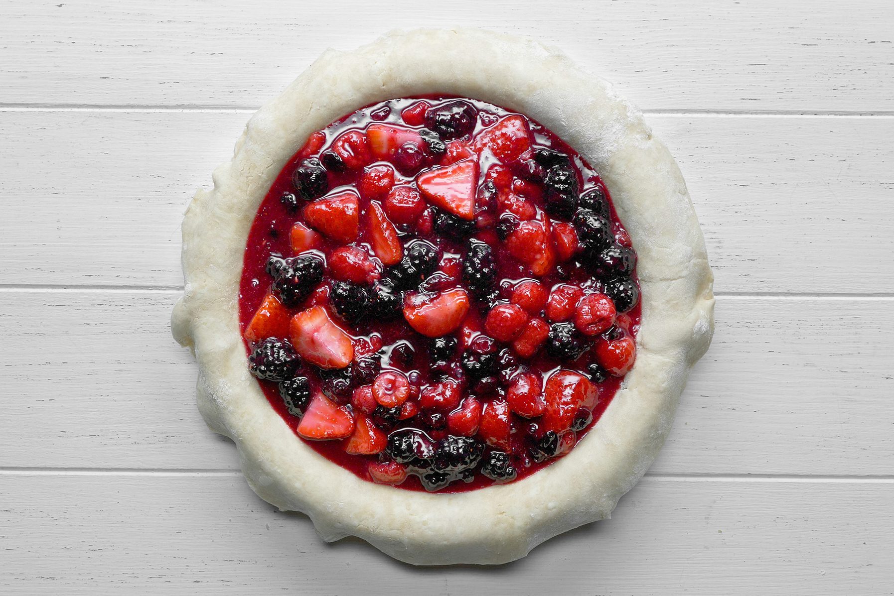 An unbaked fruit tart sits on a light wooden surface.