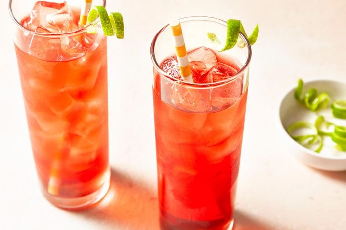 High angle view shot of Vodka Cranberry; placed ice a highball glass; poured the vodka and cranberry juice into the glassgarnished with lime twist; straws; light pink background;
