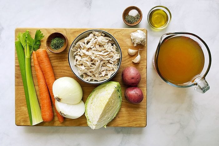 Ingredients for cooking Taste of Home's Chicken Cabbage Soup on a cutting board and white marble background