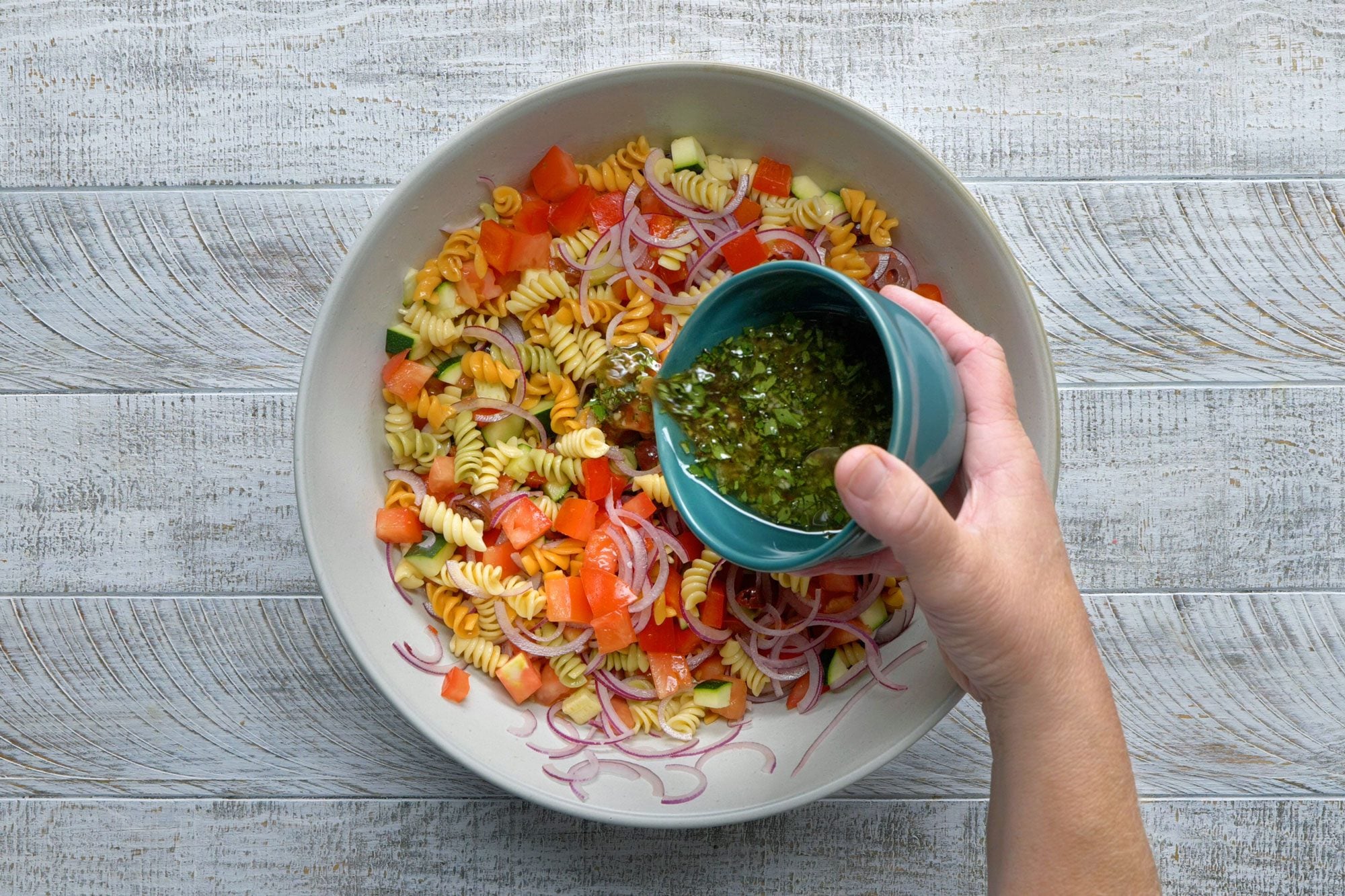 Add vinaigrette in the pasta and vegetable mix; wooden background;