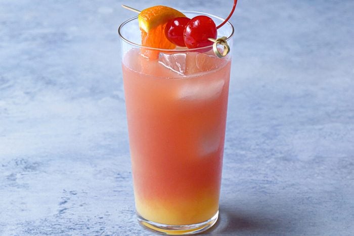 horizontal shot; blue textured background; sex on the beach served in glass, garnished with orange wedge and maraschino cherry