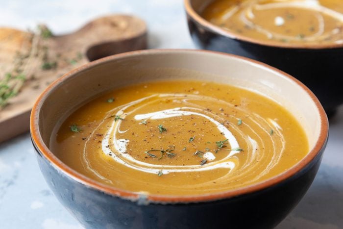 two single servings of butternut squash soup with a sour cream and fresh thyme garnish