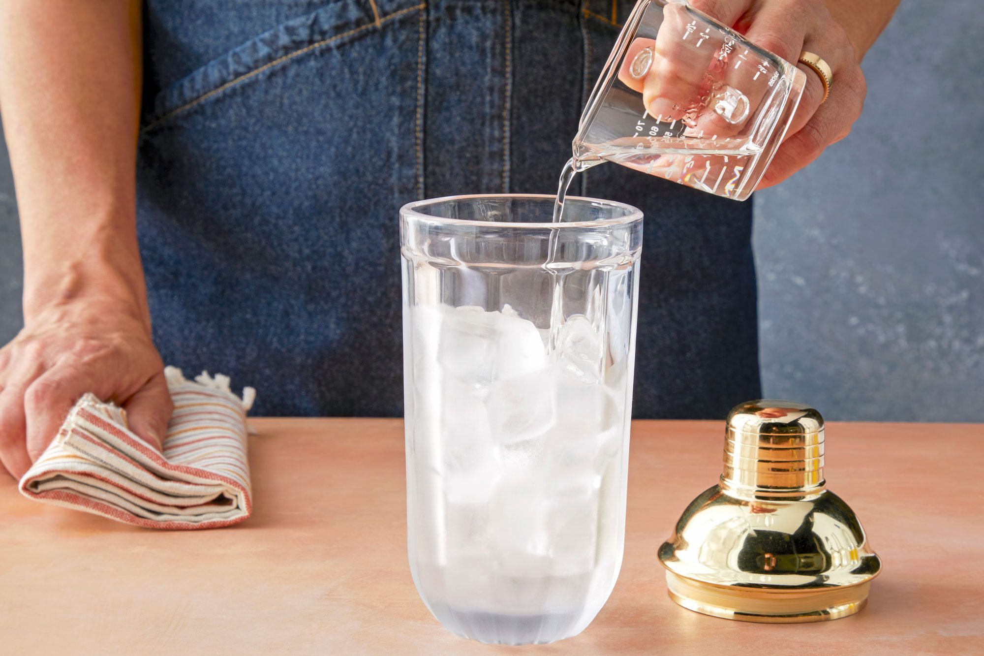 Table view shot of fill a shaker half full with ice; add vodka; kitchen towel; light orange background;
