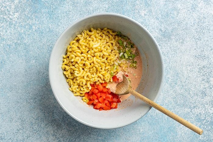 overhead shot of macaroni, tomatoes, green onions and dressing in a large serving bowl