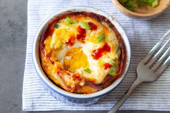 Taste of Home Bacon and Egg Muffins in blue ramekins, topped with green onions cheese, wooden bowl of green onions, forks