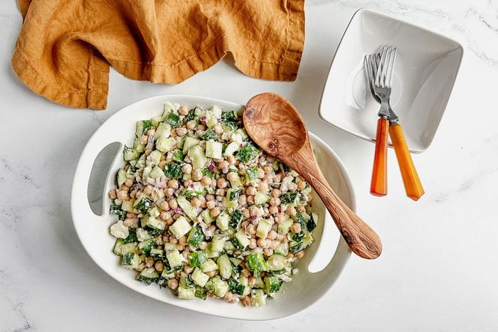 Taste of Home chickpea cucumber salad in a white ceramic bowl with linen napkin on a marble surface.