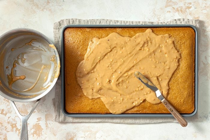 overhead shot; white textured background; Spooning glaze mixture over warm cake, spreading evenly with spreader;