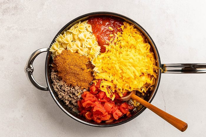 Overhead shot of cooked pasta, onion,crumbled beef,cheese, salsa, tomatoes and taco seasoning in a large skillet