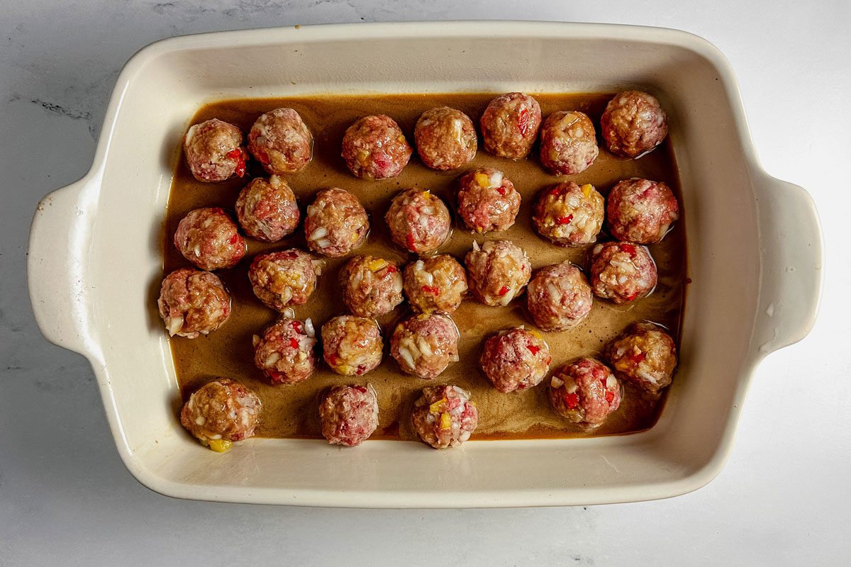 Unbaked Taste of Home teriyaki meatballs in a white ceramic baking dish on a marble surface