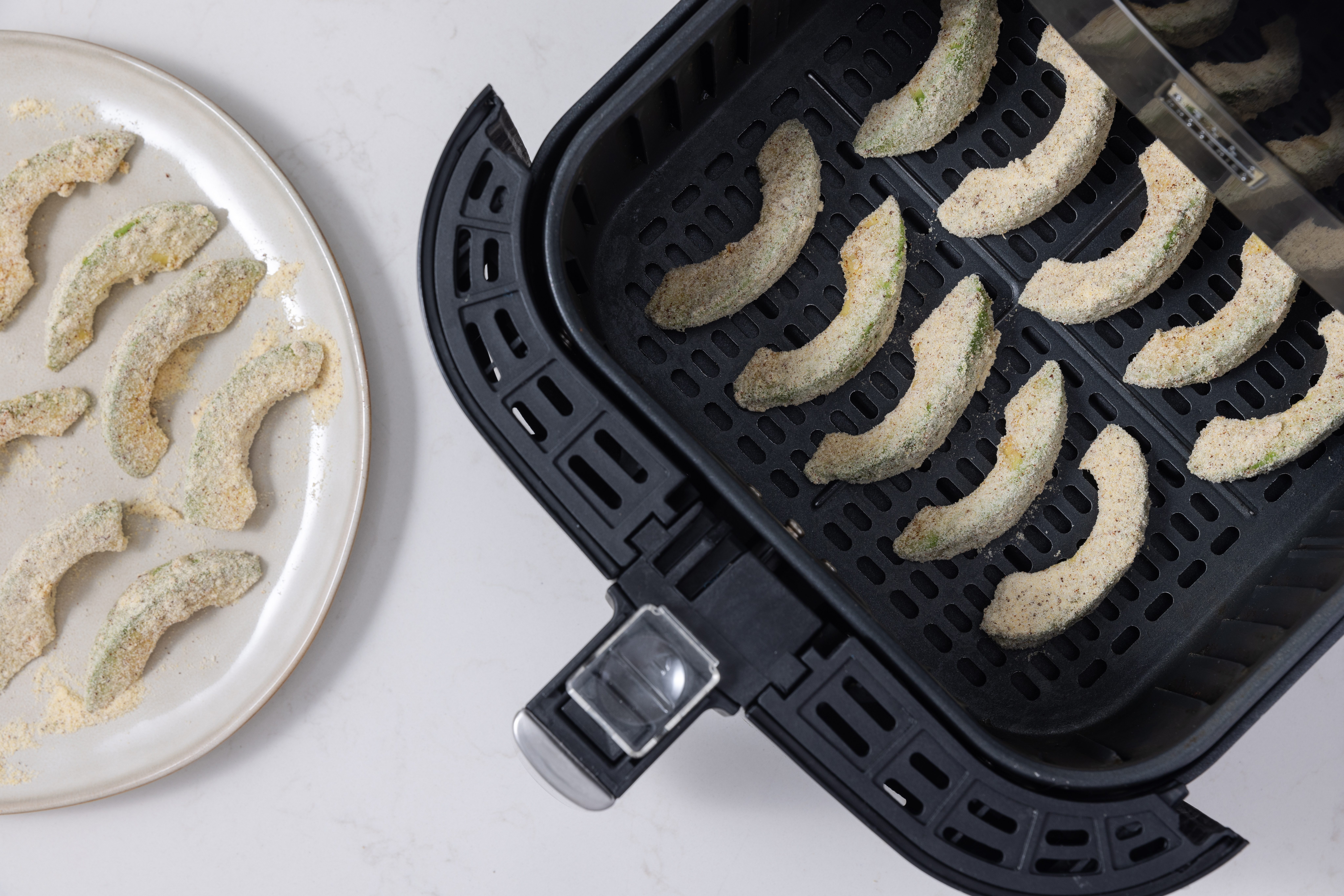 Avocado slices being placed in airfryer basket.