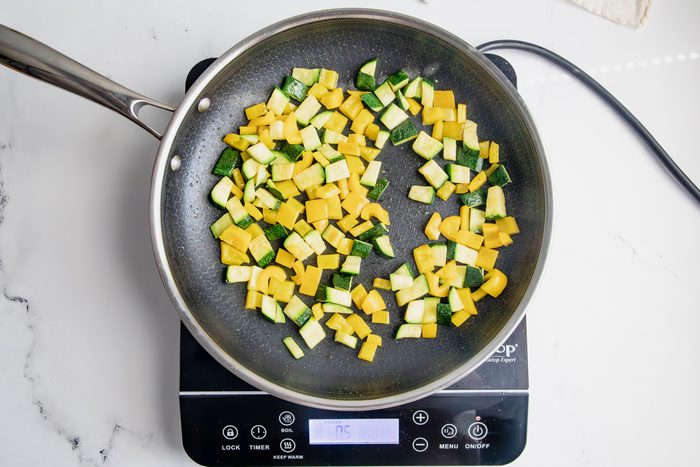 Peppers and zucchini cooking in a skillet on an induction cooktop for Taste of Home Pesto Gnocchi on a marble surface.