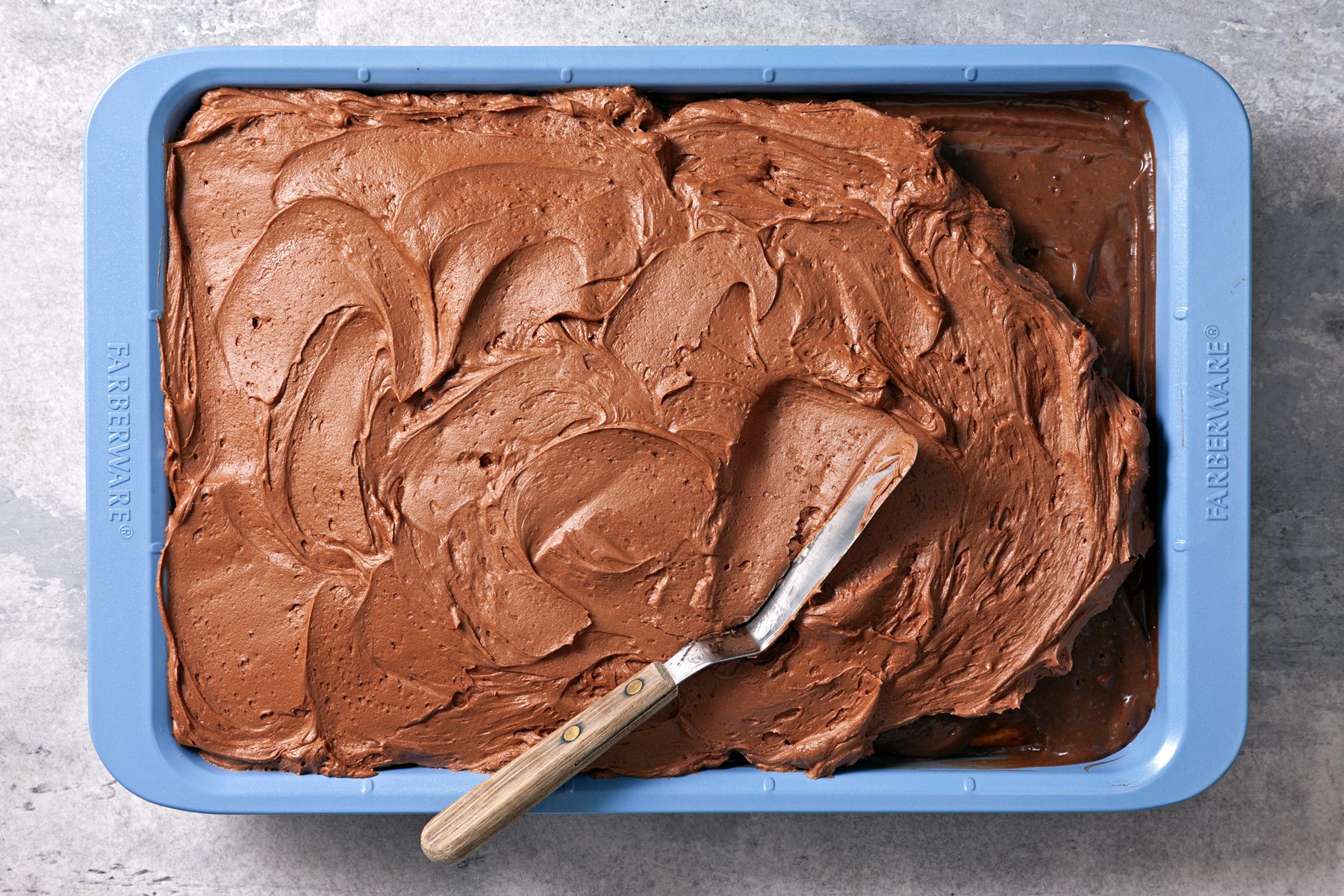 Overhead shot of baking pan; gently spread over cake; grey surface