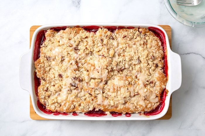 Baked Raspberry coffee cake in baking dish with drizzled vanilla glaze for step four of Raspberry Coffee Cake recipe for Taste of Home