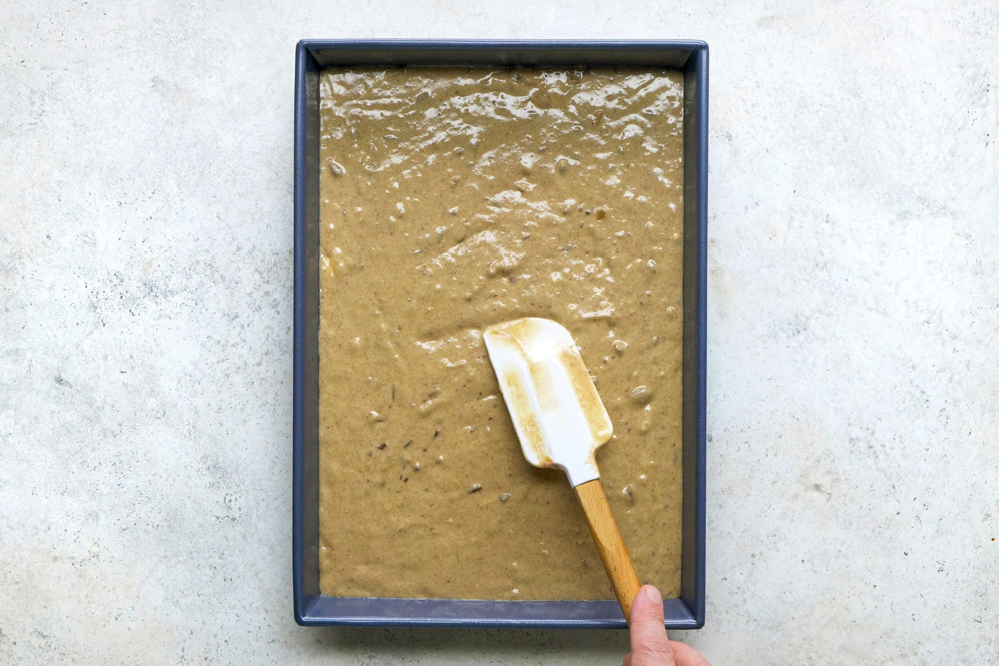 Overhead shot of transfer to a greased baking pan; bake until a toothpick inserted in center comes out clean; spatula; marble surface;