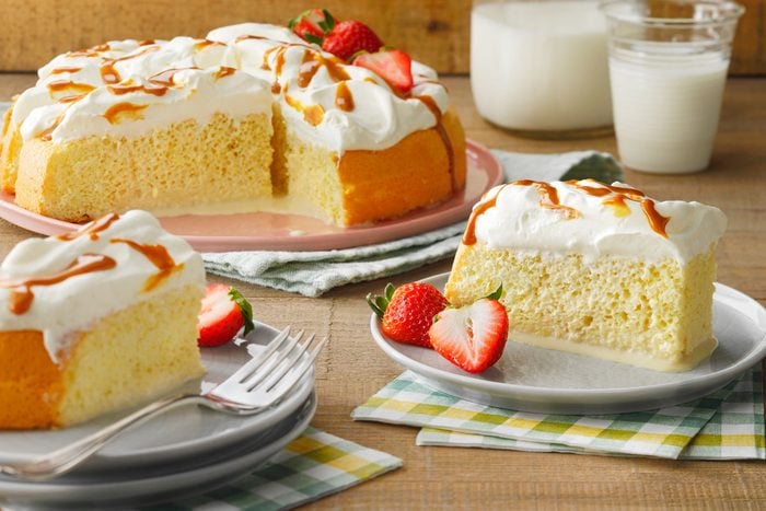 two slices of Tres Leches Cake served on plates with the full cake on a serving plate in the background