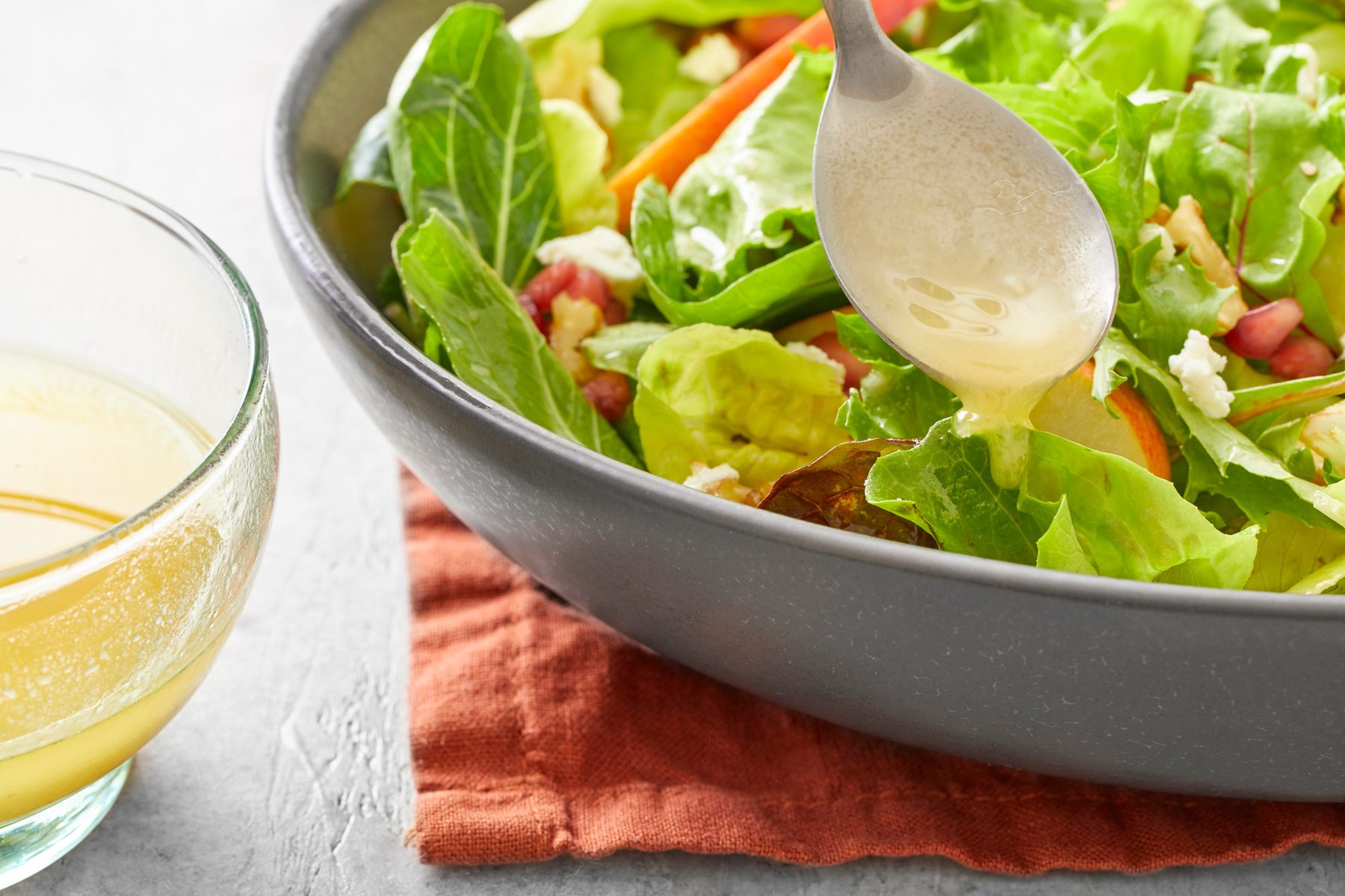 Close shot of Champagne Vinaigrette; served over salad bowl; napkin; spoon; grey background.