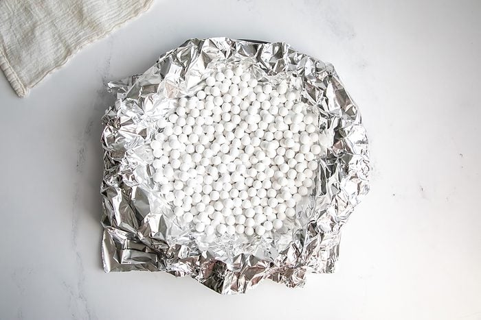 Overhead shot for Taste of Home Fudge Pie, unbaked crust in a pie tin with tin foil and pie beads.