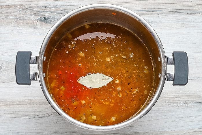 The lentils, broth, crushed tomatoes., seasonings and bay leaf are added to the Instant Pot in preparation for pressure cooking.