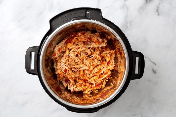 Cooked and shredded chicken breasts in an pressure cooker for step two of Instant Pot Salsa Chicken recipe for Taste of Home