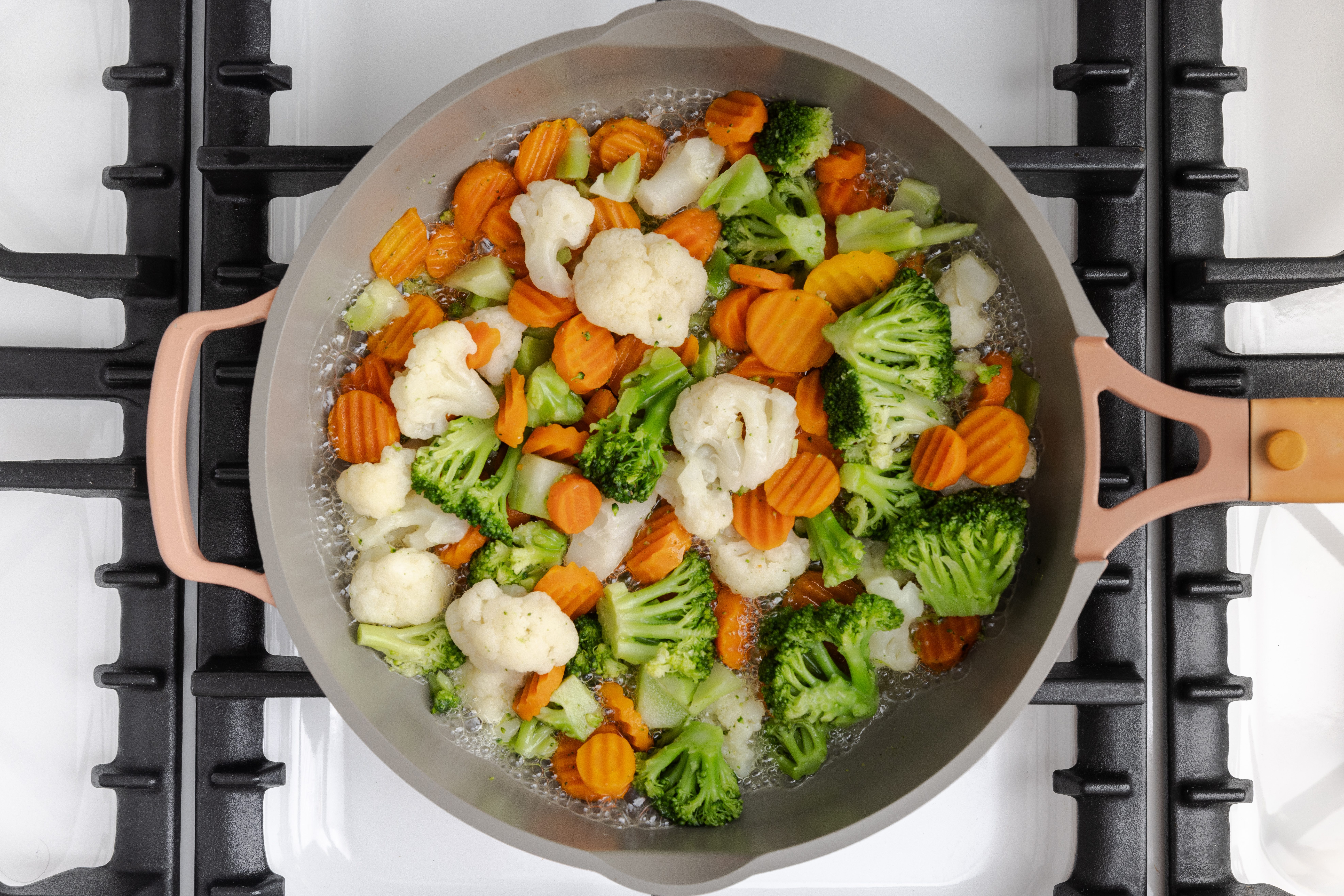 Vegetables being brought to a boil with water in skillet.