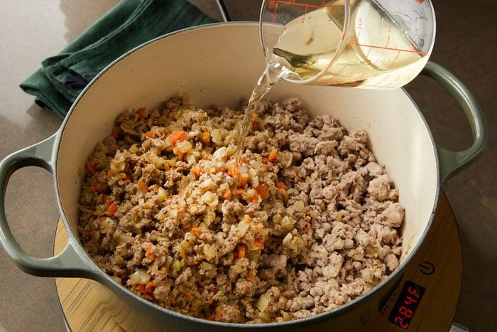 Adding broth to crumbles of sausage and beef with vegetables to prepare Pappardelle Bolognese in a pan