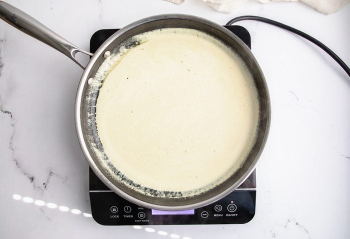 Overhead shot for Taste of Home Pork Chops and Noodles, creamy sauce cooking over an induction cooktop.