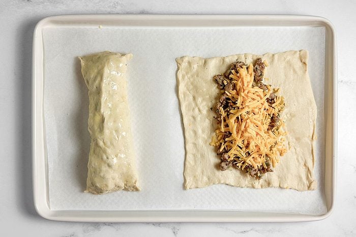 Rolled and unrolled Taste of Home Sausage Crescent Rolls on a white baking sheet