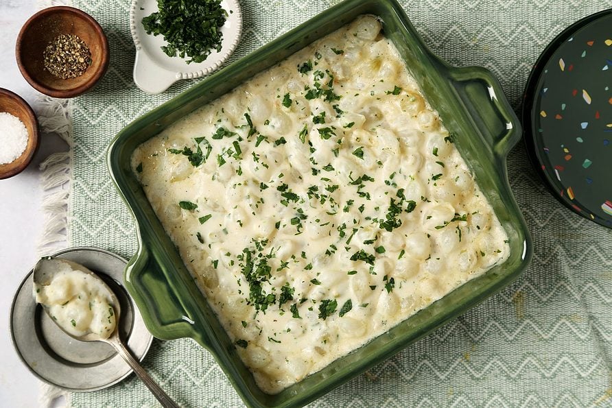 Close up of Taste of Home's Creamed Pearl Onions in a green casserole dish on a grey marble surface.