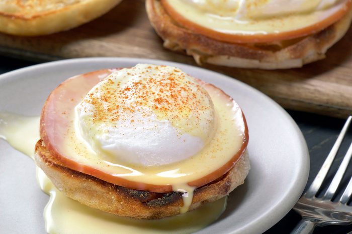 Eggs Benedict served in a white plate with fork on side