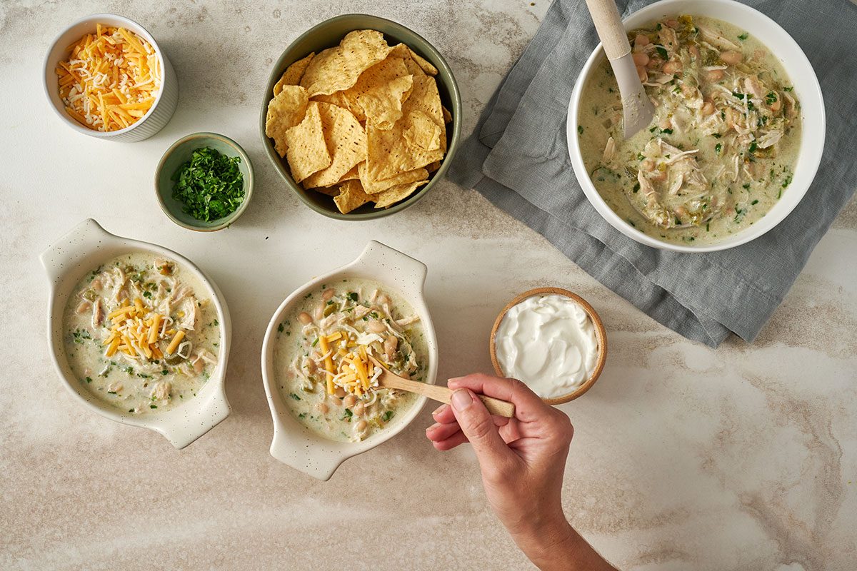 Overhead view of the fully cooked Taste of Home Green Chicken Chili served in a bowl with optional toppings of shredded cheese, sour cream, and crushed tortilla chips.