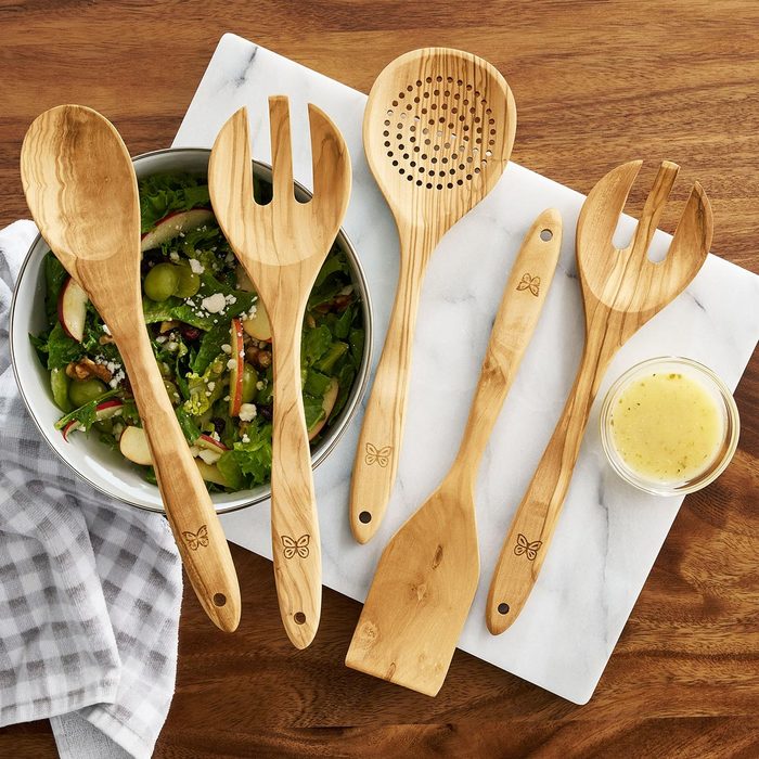 Five wooden stirring utensils sit on top of a wooden counter top