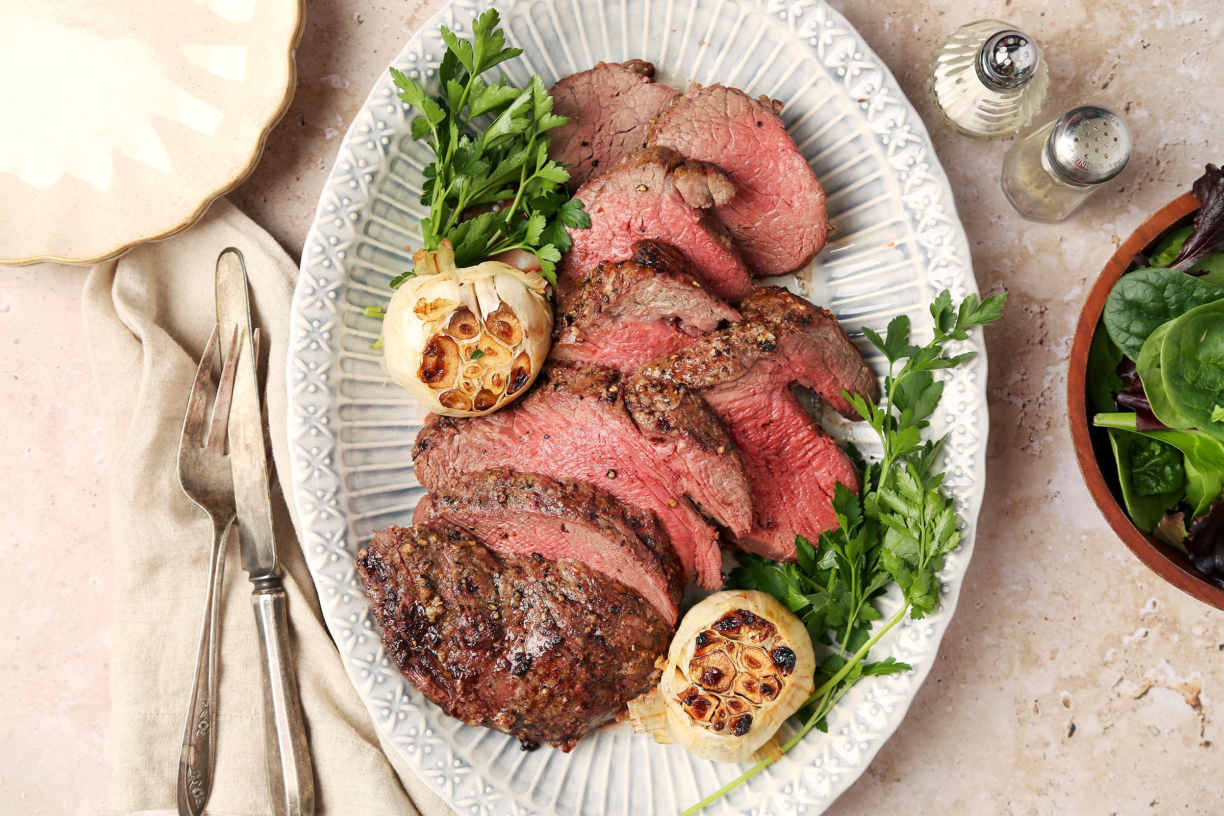 Beef Tenderloin Roast on a plate with roasted garlic and greens on side