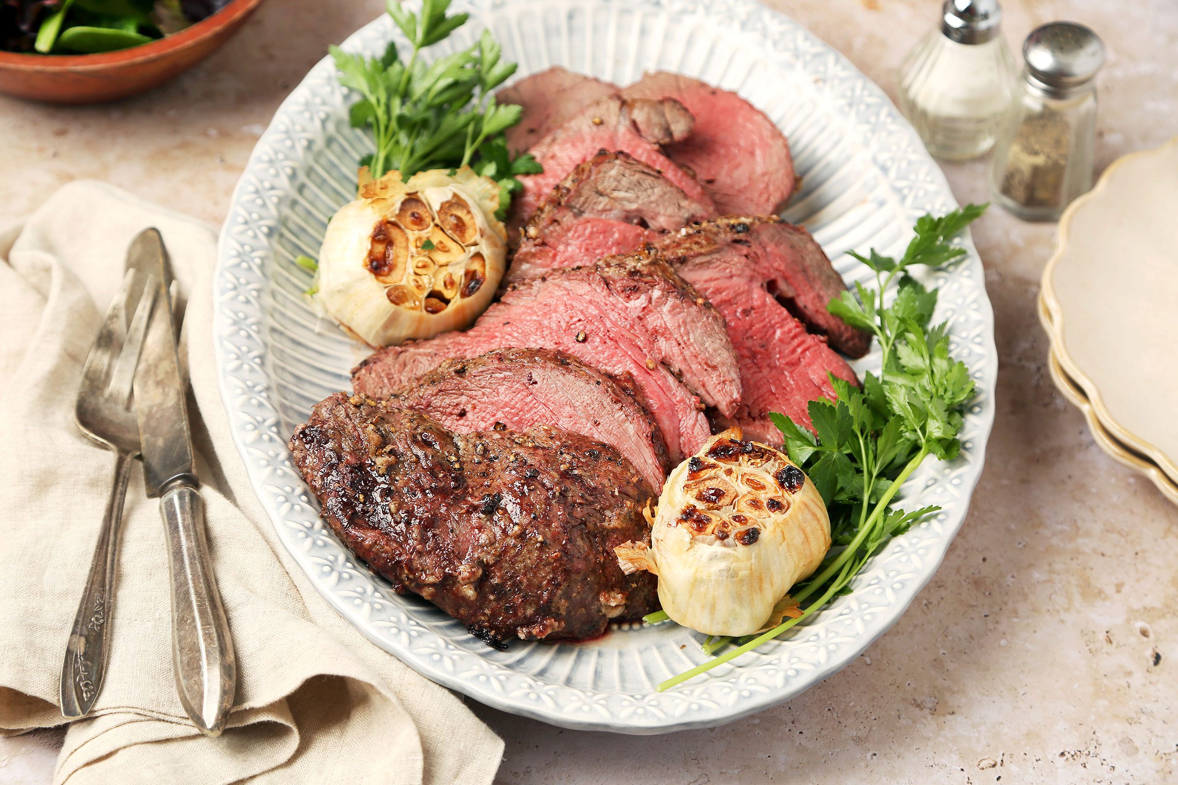 Beef Tenderloin Roast on a plate with roasted garlic and greens on side