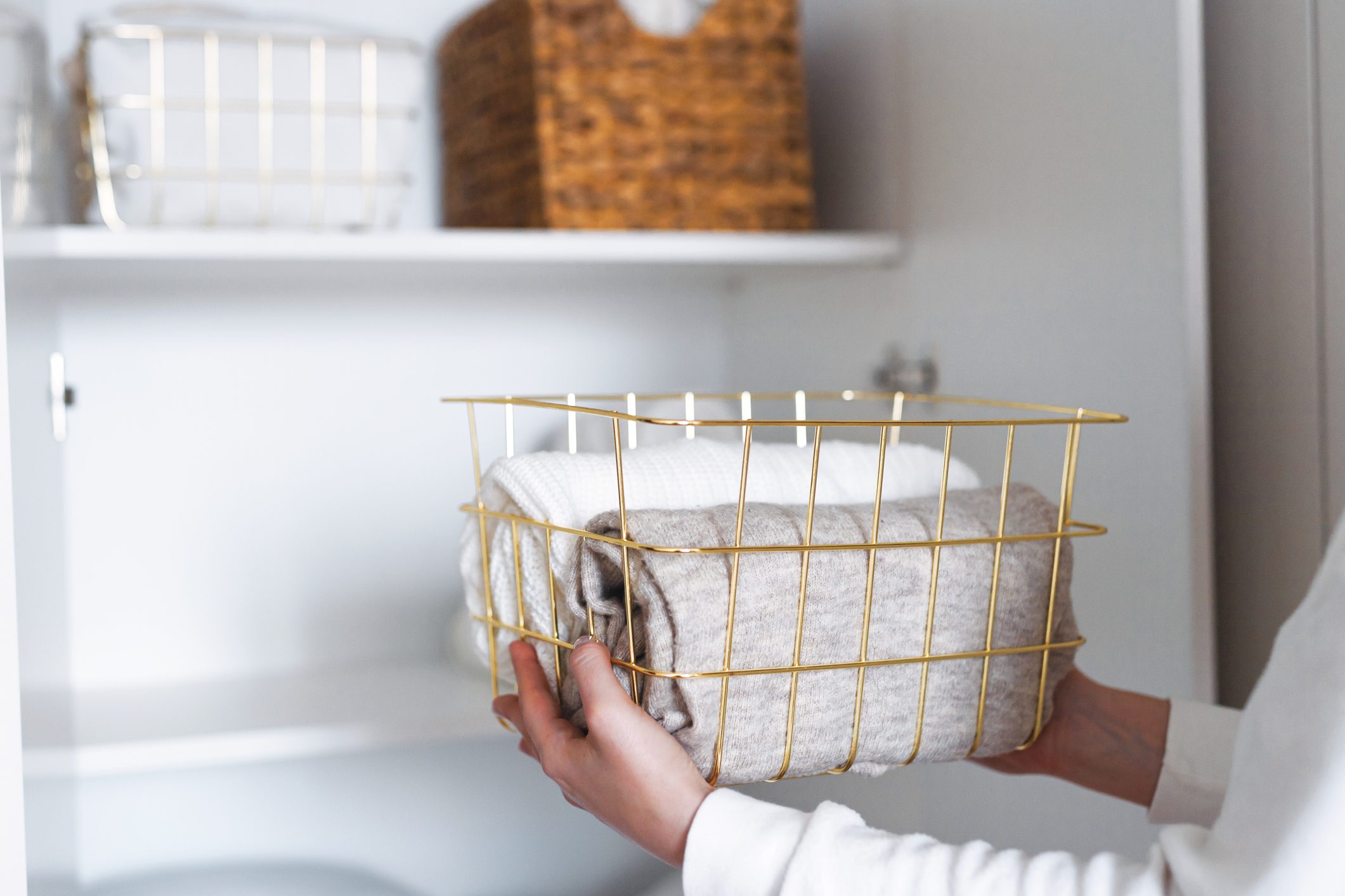 Woman organizing clothes on shelves in white wardrobe, folding laundry in baskets. Space organization and storage system