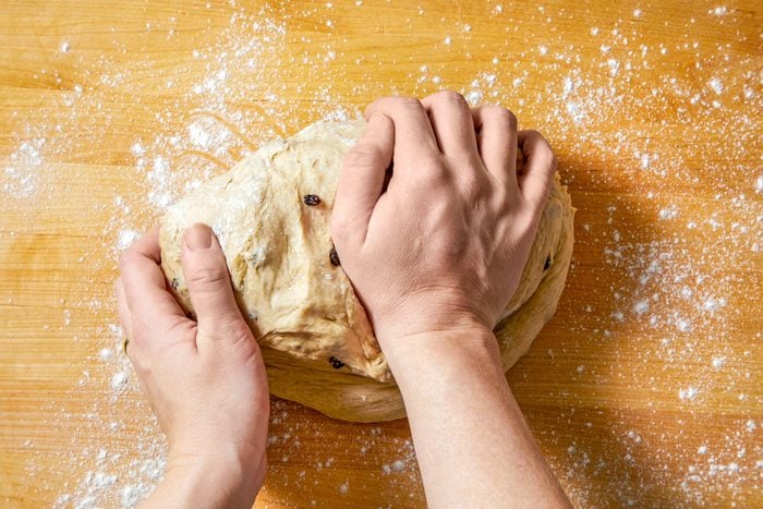 overhead shot of a pair of hands kneading a dough on a wooden surface, the surface is dusted with flour