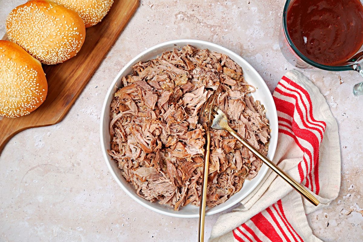 Cooked pork pulled apart with forks in a white bowl.