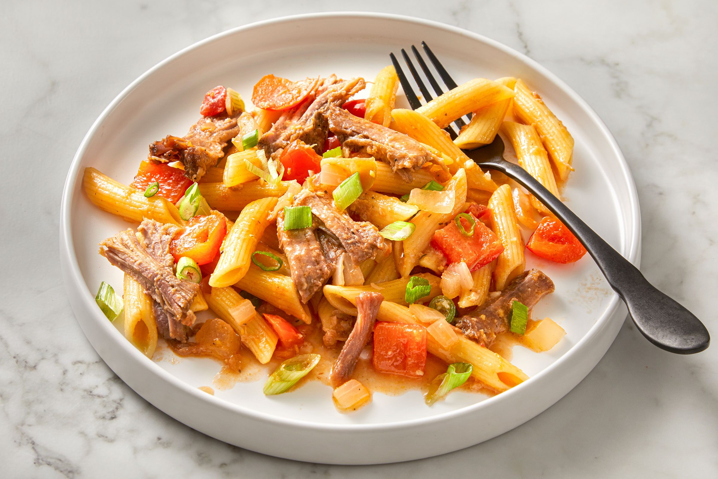 Barbecue Pork And Penne pasta on a white plate with a fork in it