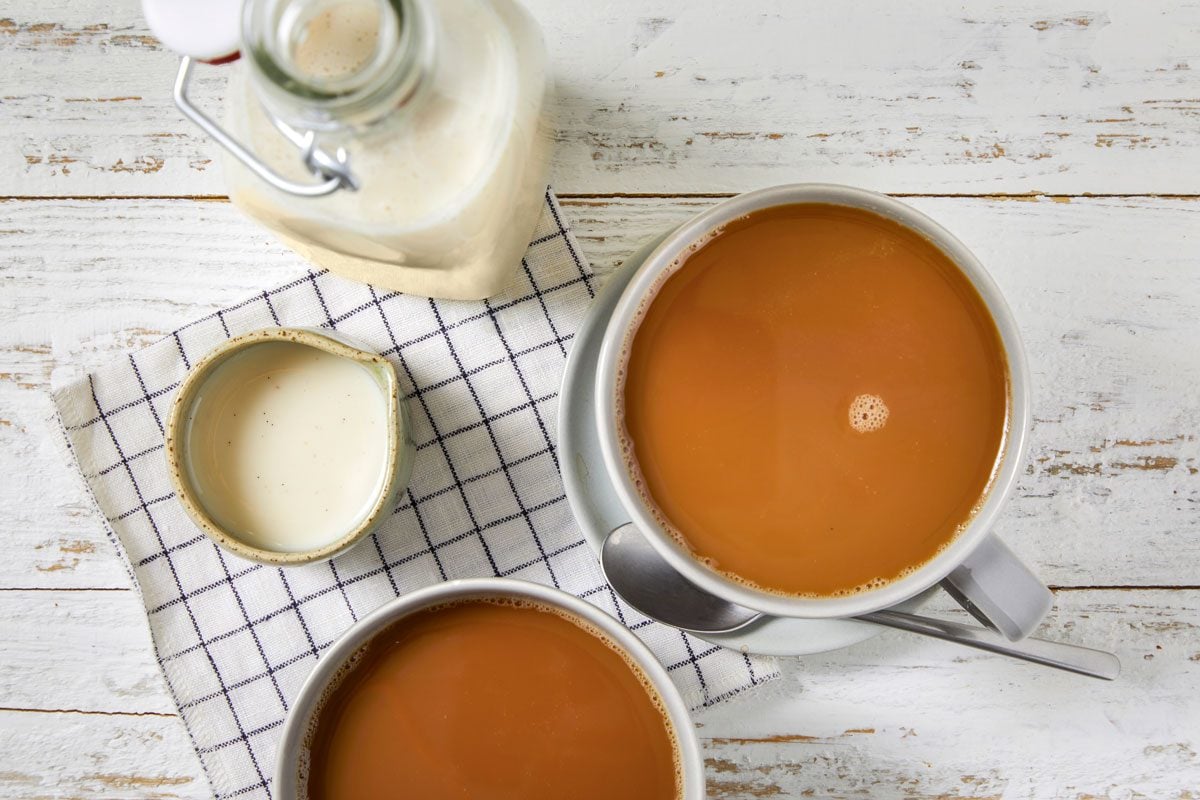 Overhead shot of Vanilla Coffee Creamer; Store in a glass container; Stir before using; two cups of coffee; spoon; napkin; wooden surface;