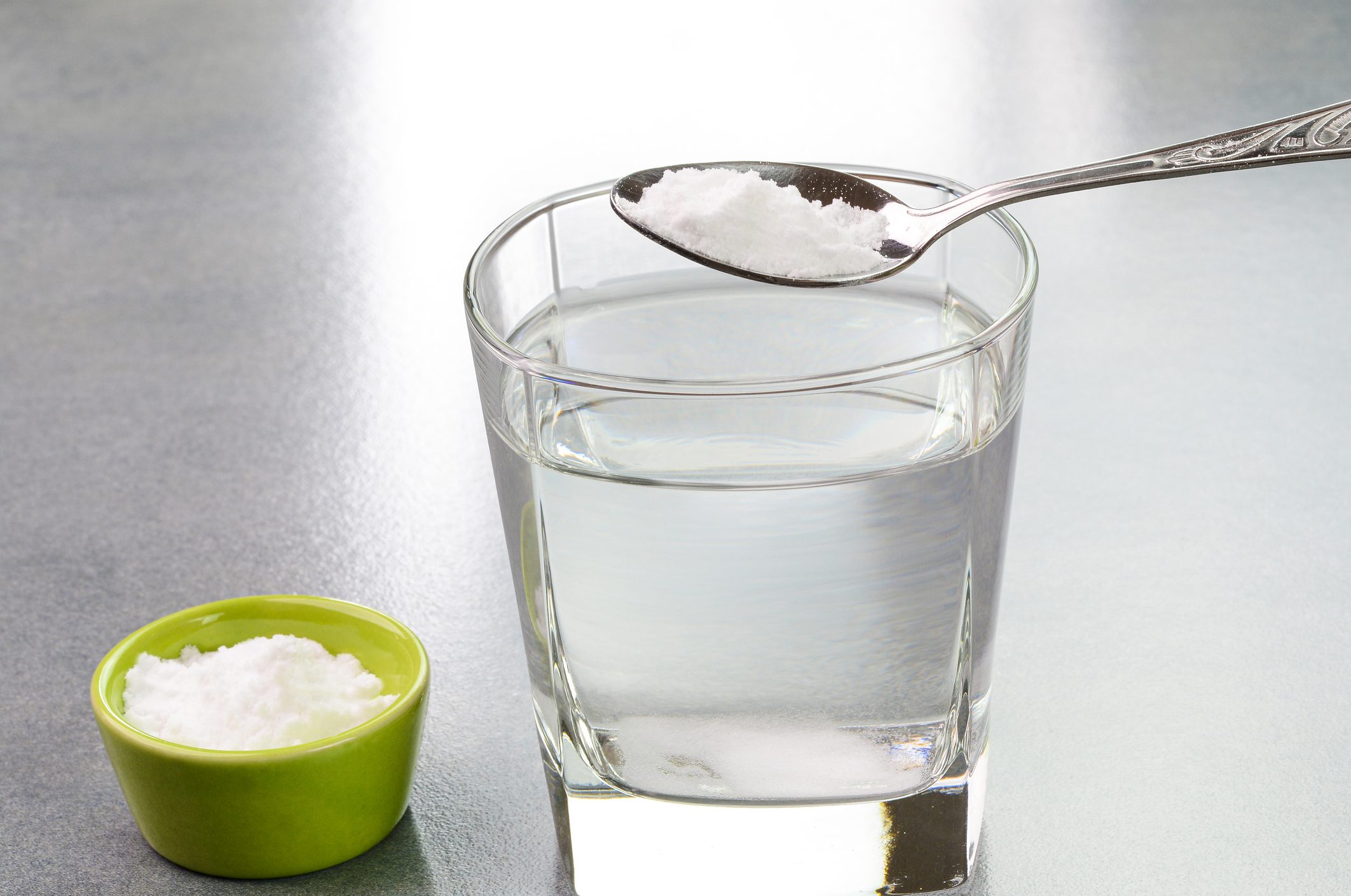 Spoonful of baking powder held above a glass of water